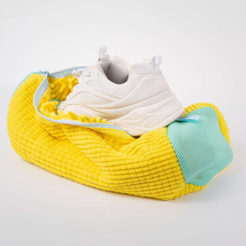 Yellow shoe bag with a white sneaker inside on a light gray background